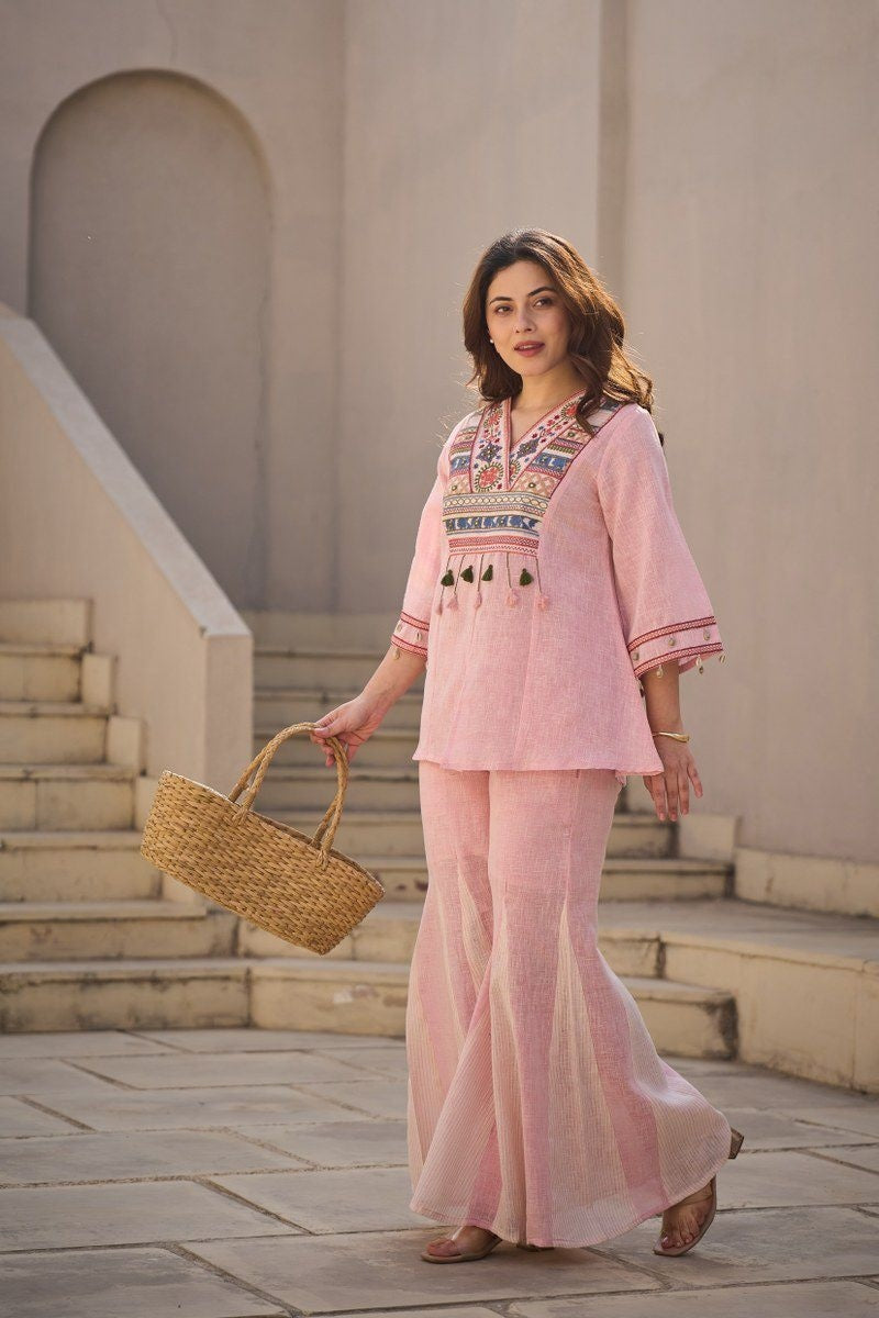 soft pink linen co-ord set featuring a tunic with intricate multi-color bib-style chest embroidery and hanging tassel details, paired with matching flared palazzos
